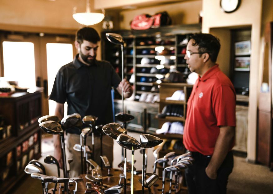 Two men examining golf clubs in a golf shop. 