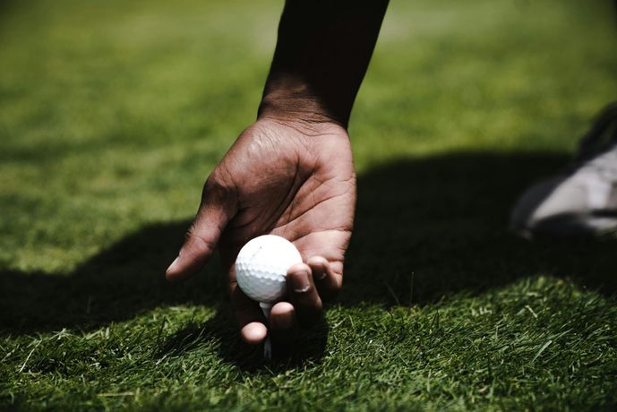 Person's hand picking up a white golf ball from green grass, outdoors.