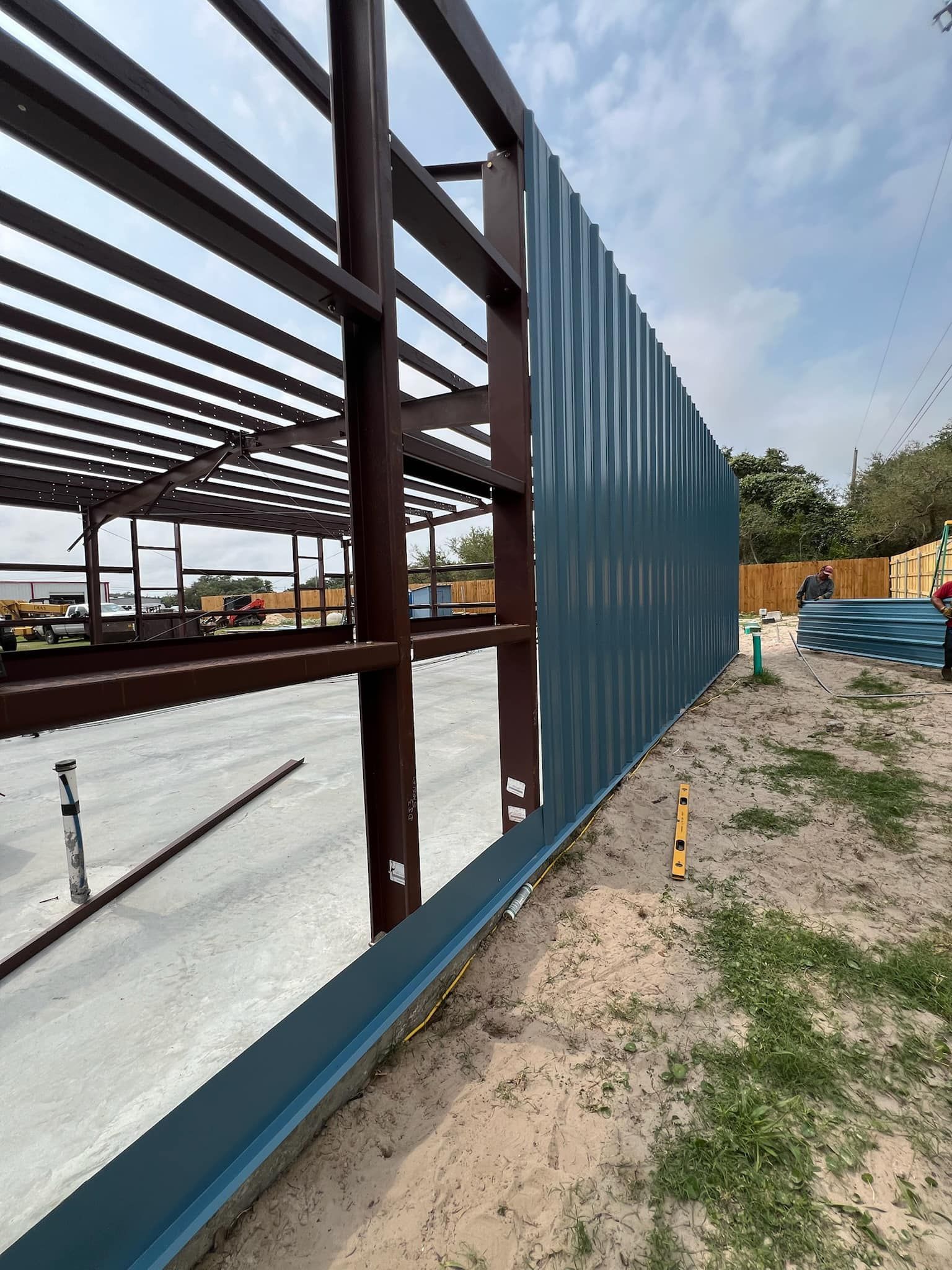 A steel building frame under construction with blue metal siding being installed on the side exterior.