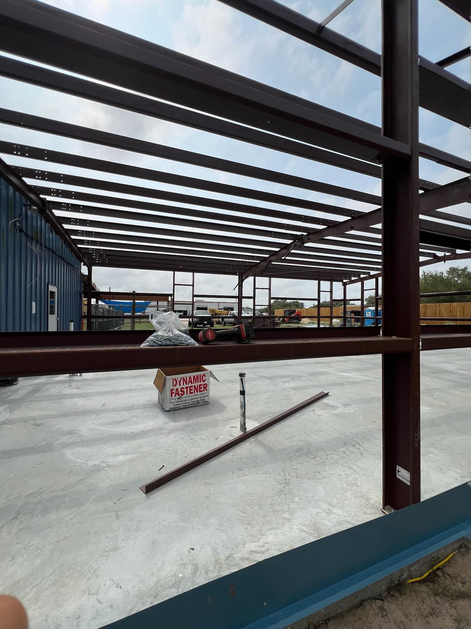Construction site with brown steel framing beams for a building structure over a concrete floor.