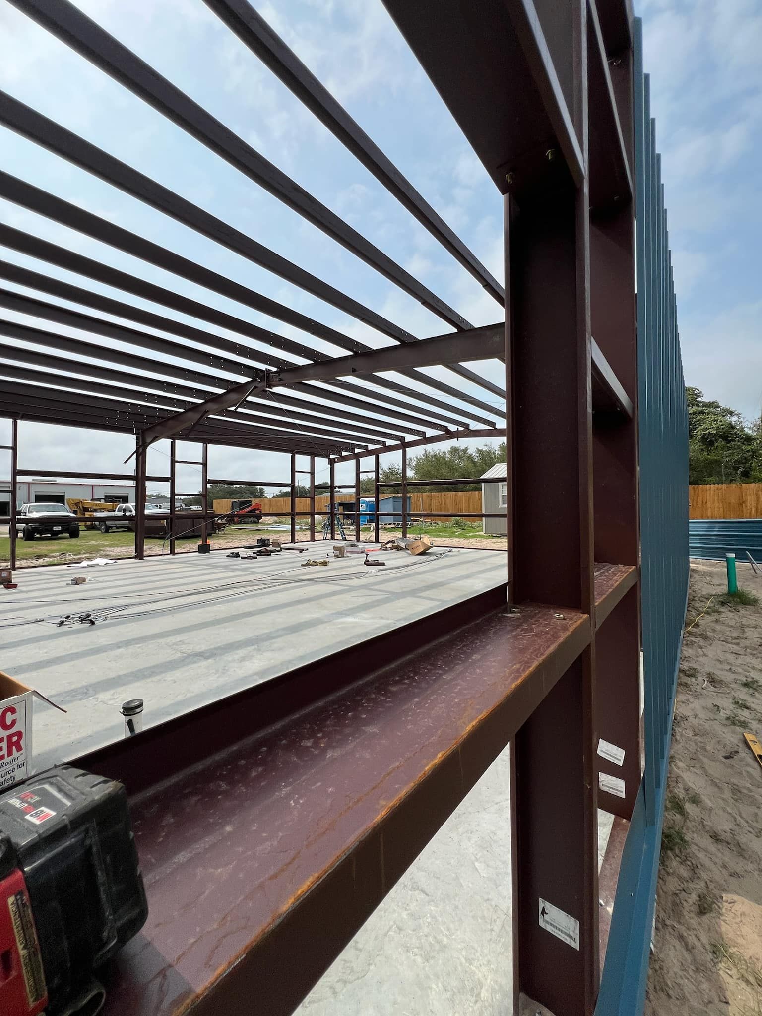 A low-angle view of the brown steel framing of a building under construction on a concrete foundation.