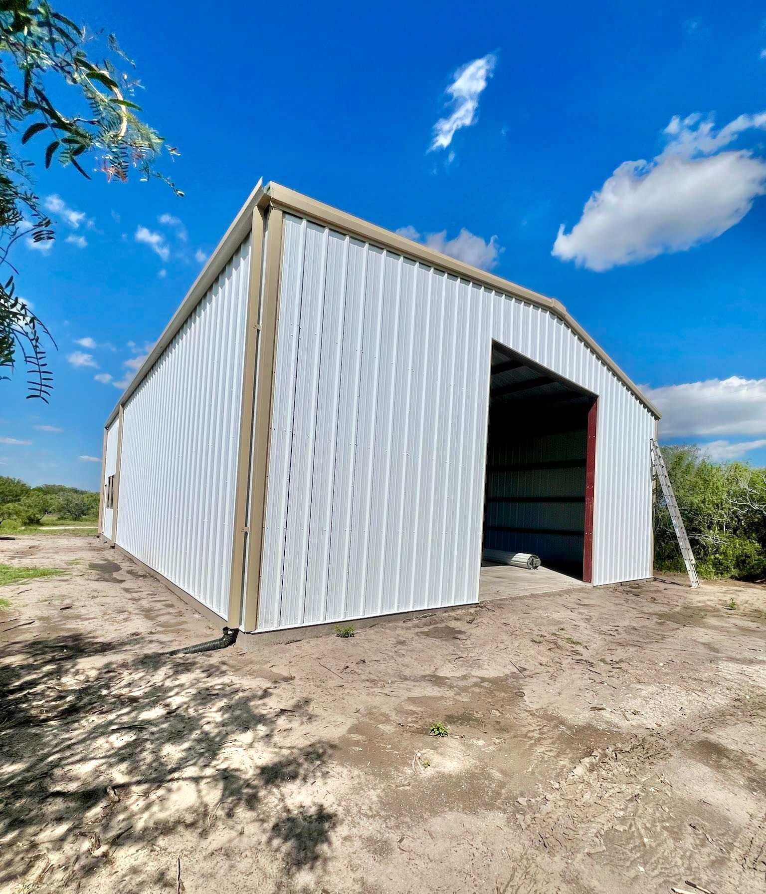 A white metal building with tan trim and an open entryway under a bright blue sky on a dirt lot.