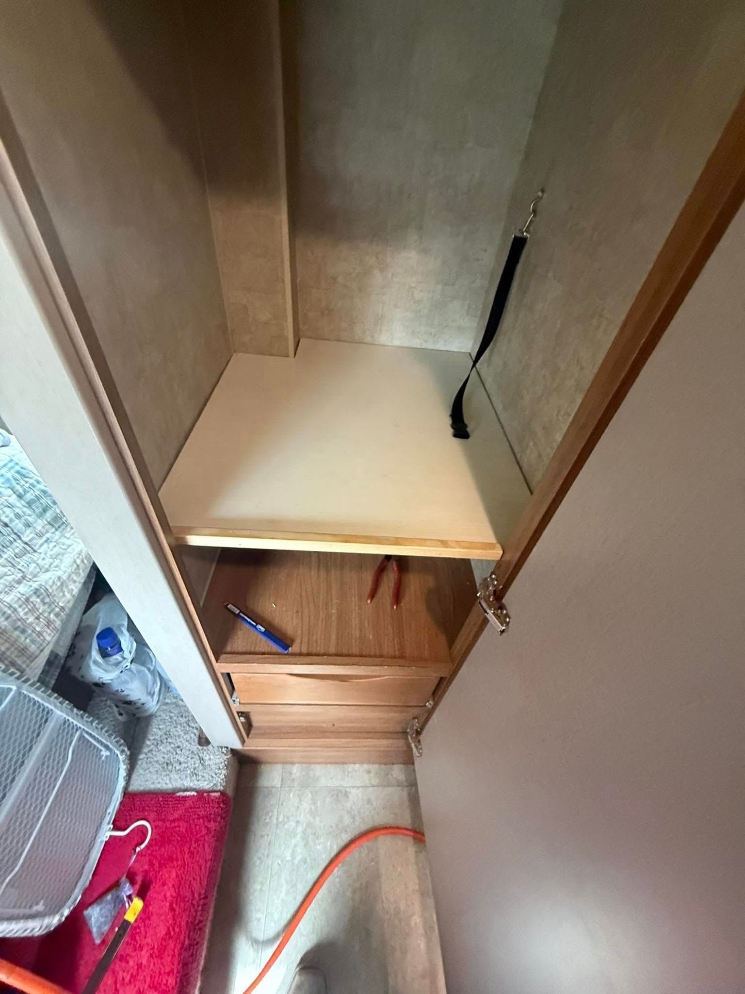 Interior of a narrow wooden closet with a single shelf installed above two drawers.