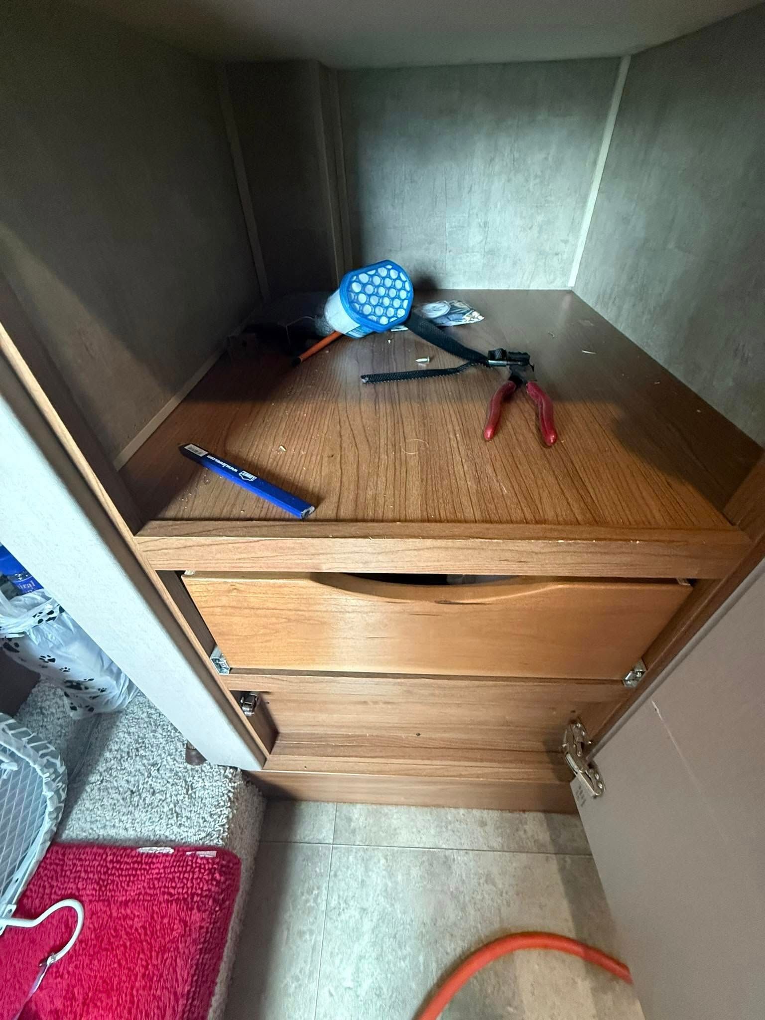 Open wooden cabinetry with a blue hairdryer, red-handled pliers, and a blue pen resting on the internal shelf.