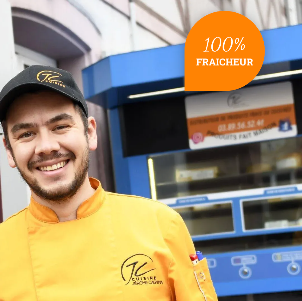 Un homme portant une veste de chef jaune sourit devant un panneau 100 % fraîcheur