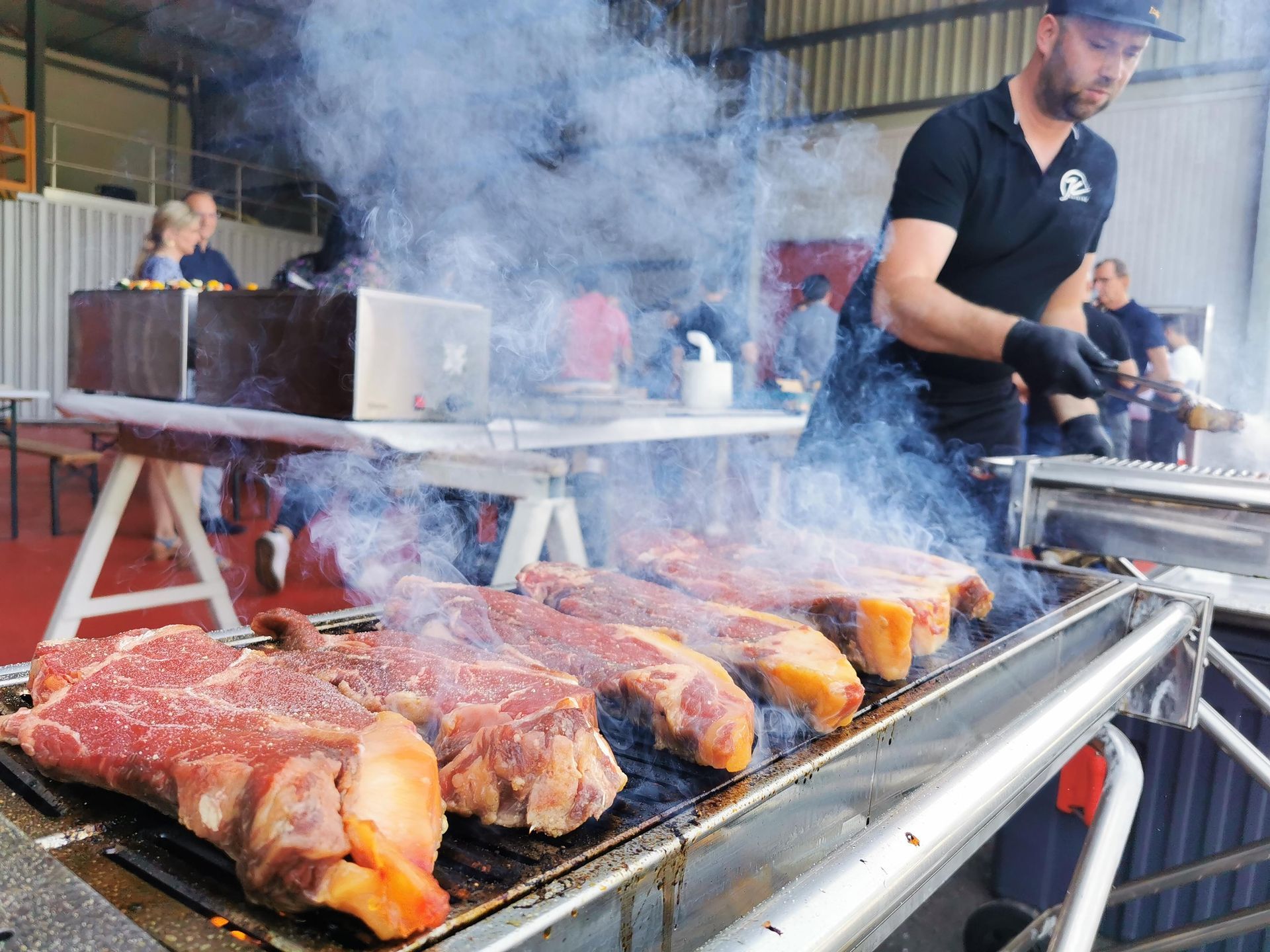 Un homme fait cuire de la viande sur un gril d'où sort de la fumée.