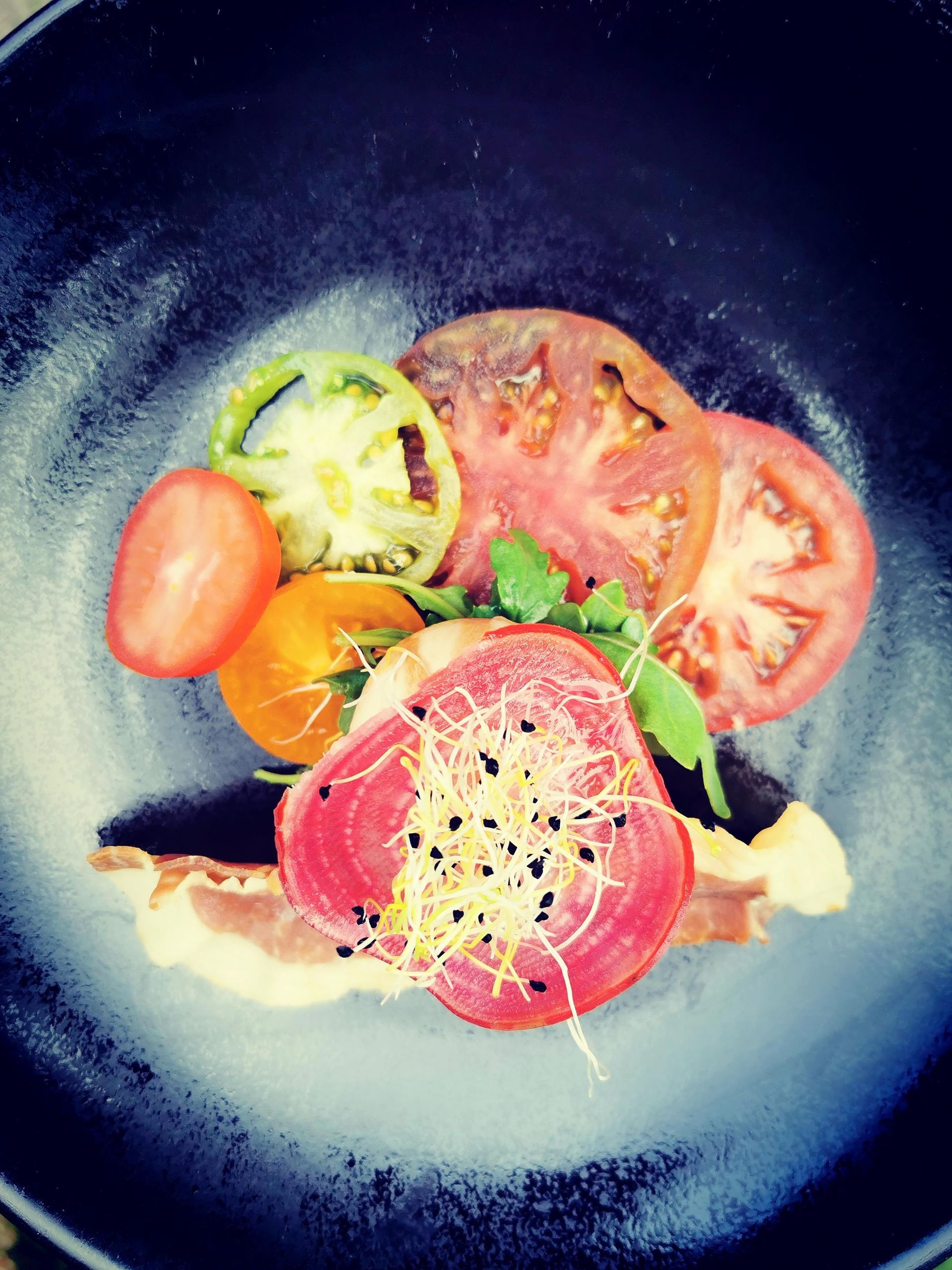 Une assiette noire garnie de tomates et d'autres légumes.