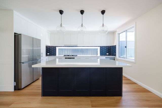 A modern kitchen features a dark blue island with a white countertop, three pendant lights, and a stainless steel fridge.