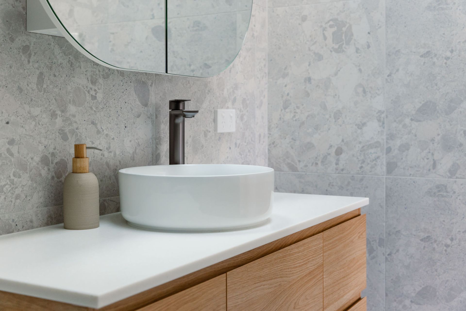 A modern, neutral-toned home features a large glass sliding door overlooking a courtyard with an olive tree and grasses.