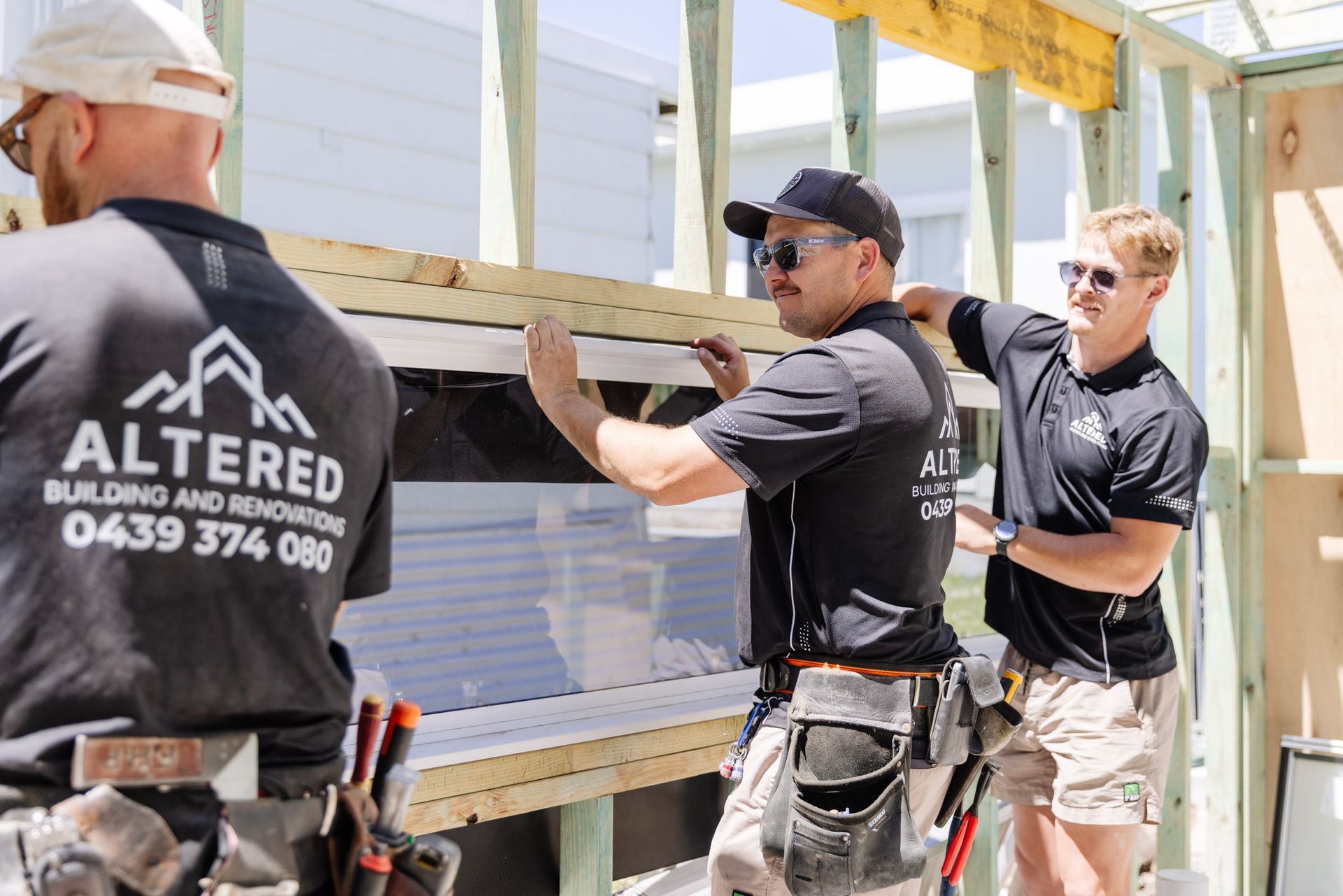 Three construction workers in black uniforms frame a wall on a building site, working together to install a window frame.