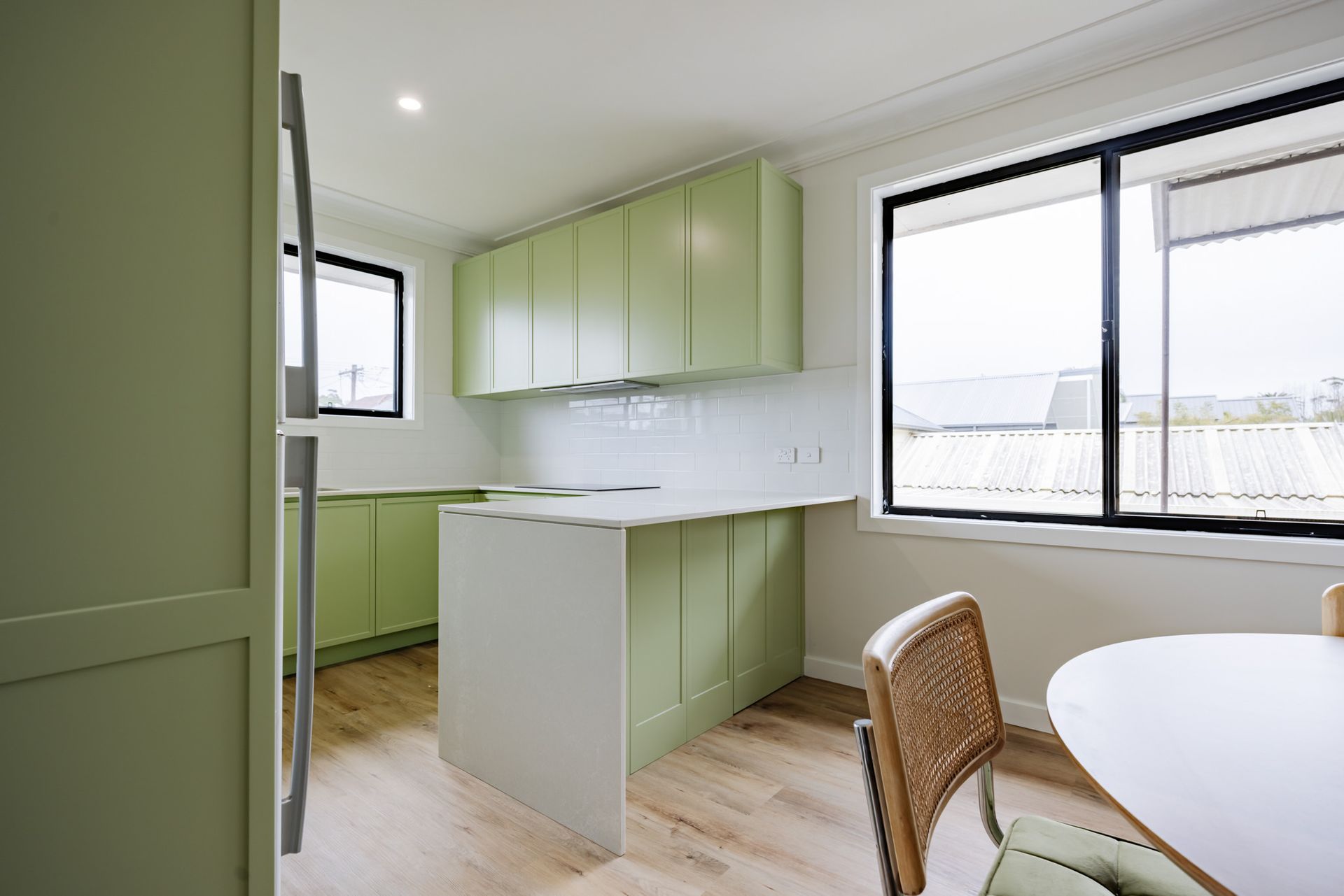 A minimalist, light-toned concrete house with flat roofs, framed by a large tree, manicured shrubs, and a stone pathway.