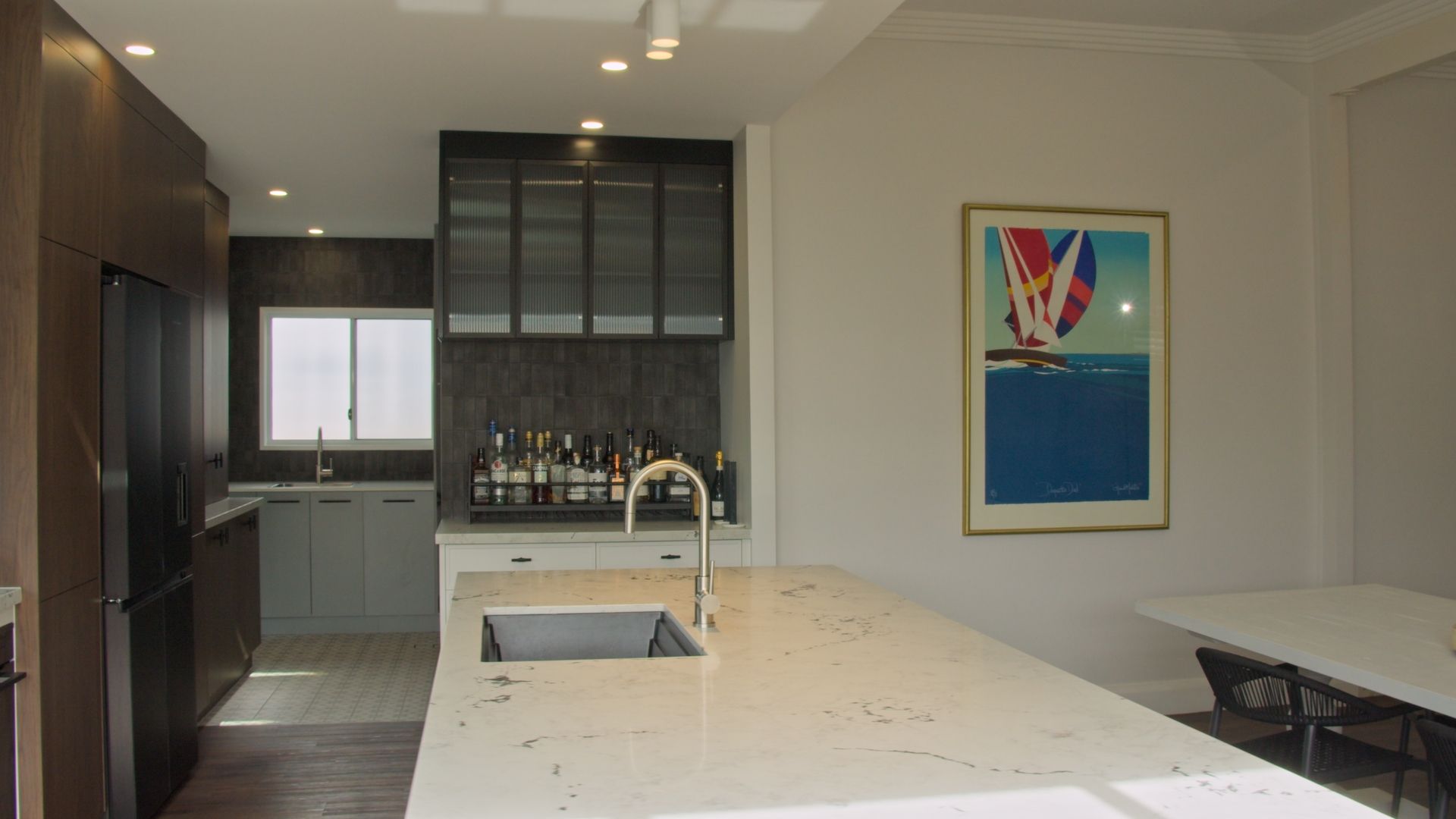 A minimalist, light-toned concrete house with flat roofs, framed by a large tree, manicured shrubs, and a stone pathway.