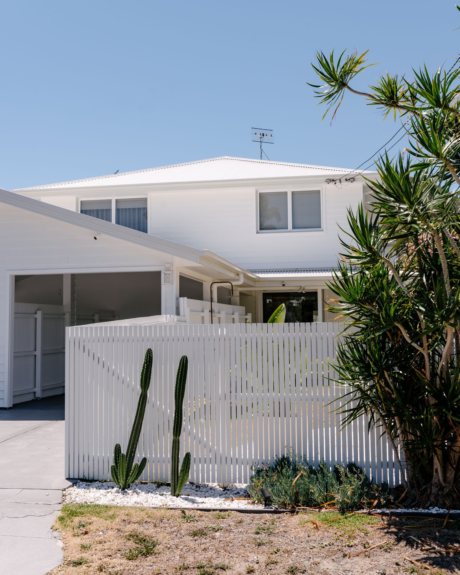 A two-story white house with a garage and a white picket fence, featuring two tall cacti in a garden bed.