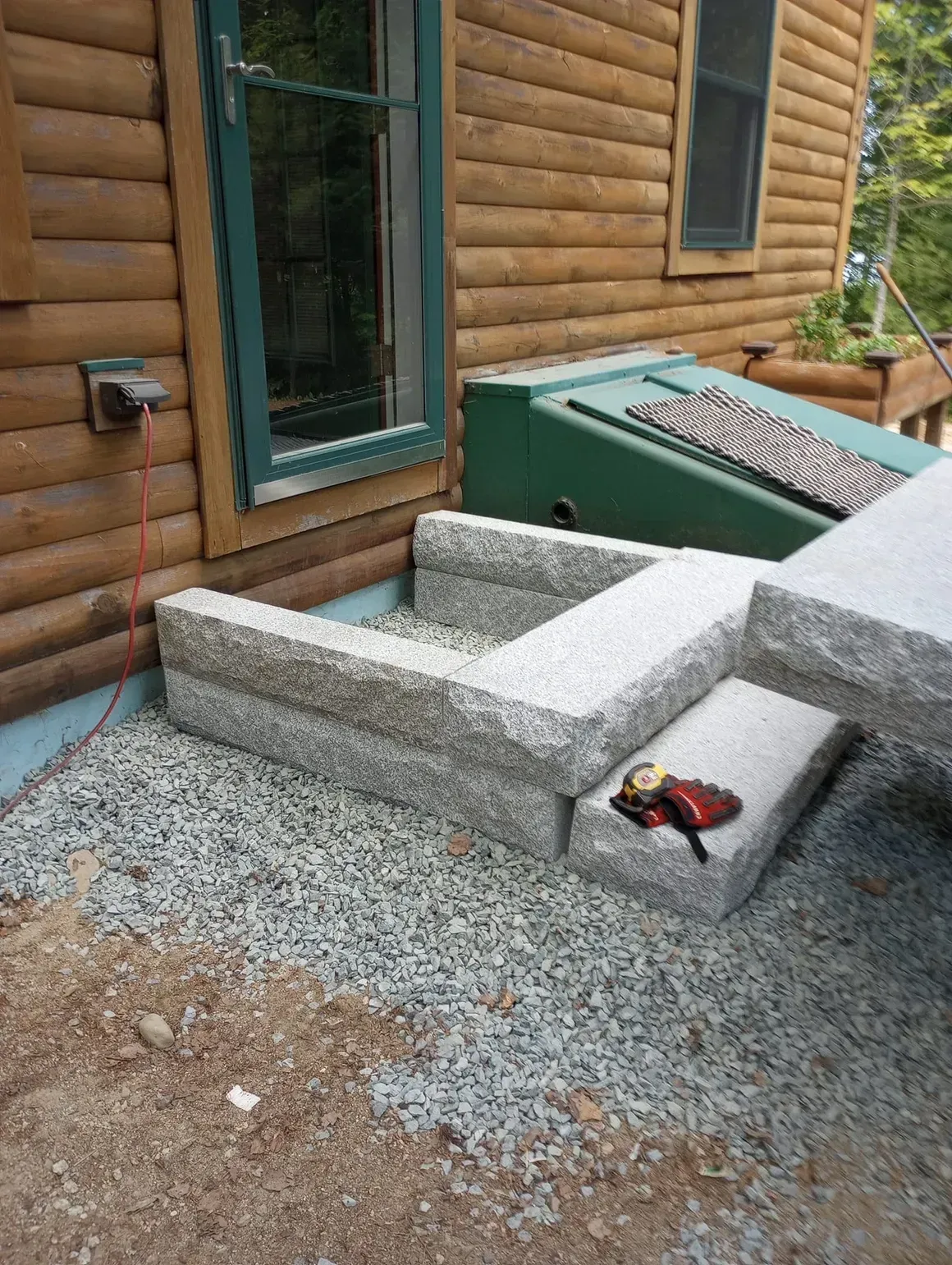 Granite steps leading up to a log cabin entrance with gravel ground cover.