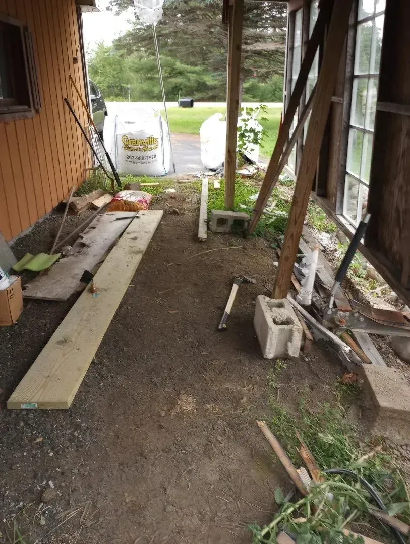 Construction area with exposed dirt, wood, and concrete blocks under a covered porch.