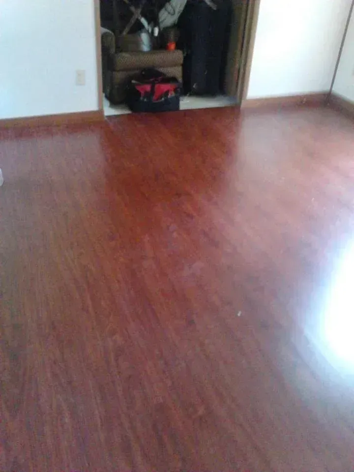 Red-toned hardwood floor in a room, leading to a doorway with items stored inside.