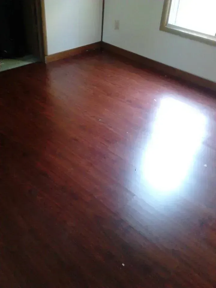 Empty room with glossy, dark wood floors and a window.