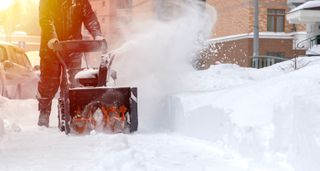 Person using a snowblower, blowing snow from a sidewalk.