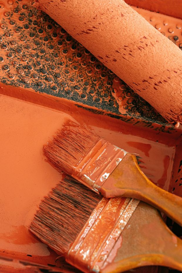 Paint brushes and roller in a tray of orange paint.