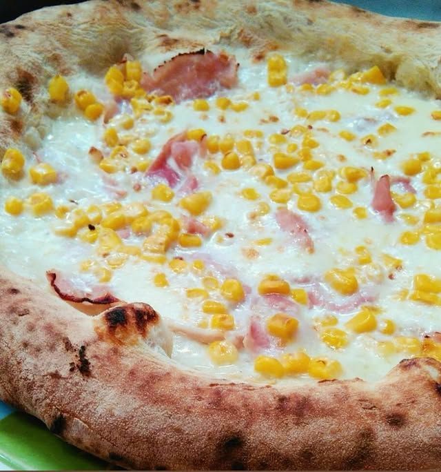 Pizza ricca di formaggio, condita con mais e prosciutto a cubetti su una crosta dorata.