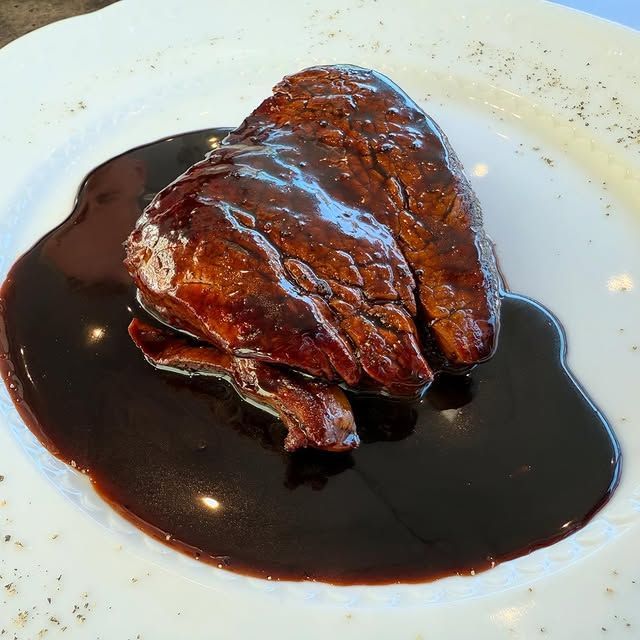 Carne lucida glassata con salsa scura su un piatto bianco.