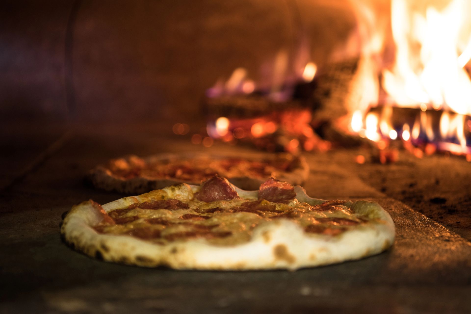 Pizza che cuoce in un forno a legna con le fiamme sullo sfondo