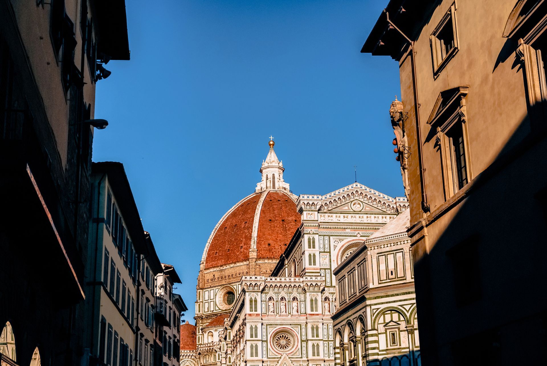 La cupola del Duomo di Firenze, incorniciata da stradine strette sotto un cielo azzurro e limpido.