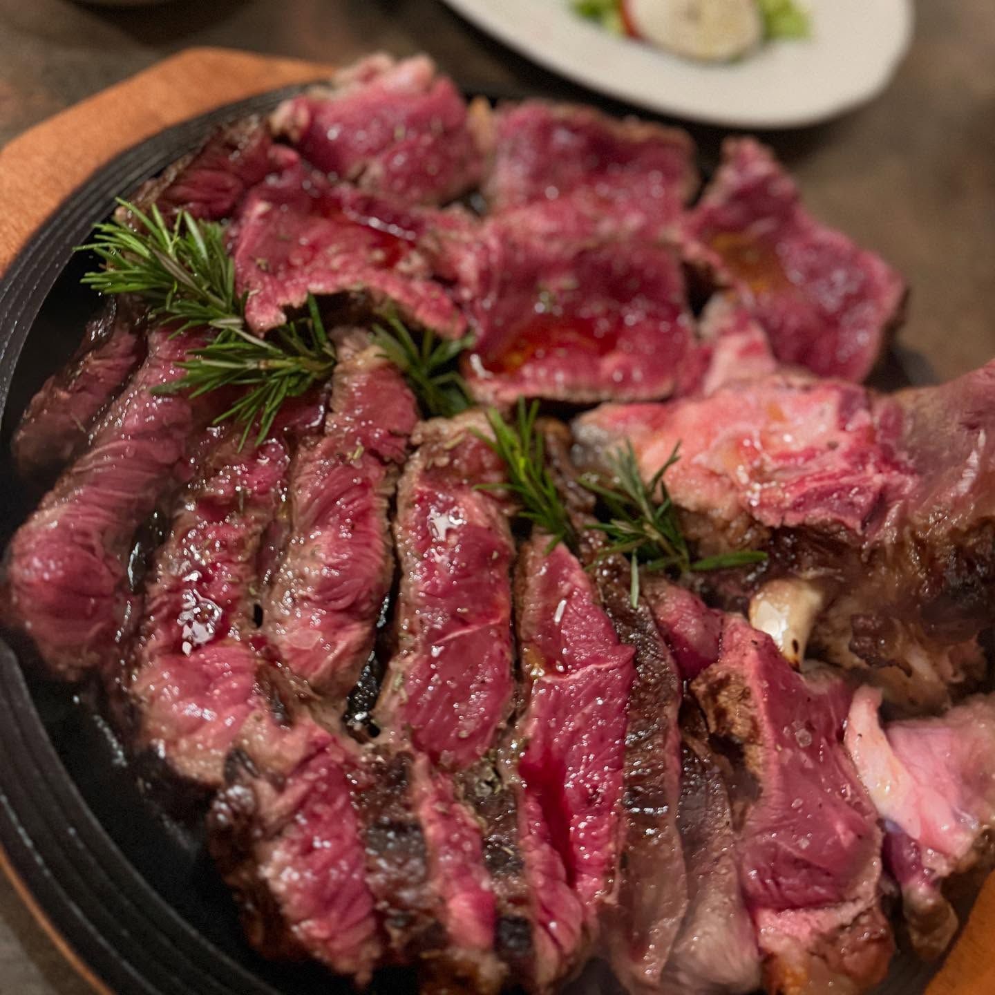 Fettine di bistecca al sangue guarnite con rosmarino su un piatto scuro, con un piccolo contorno sullo sfondo.