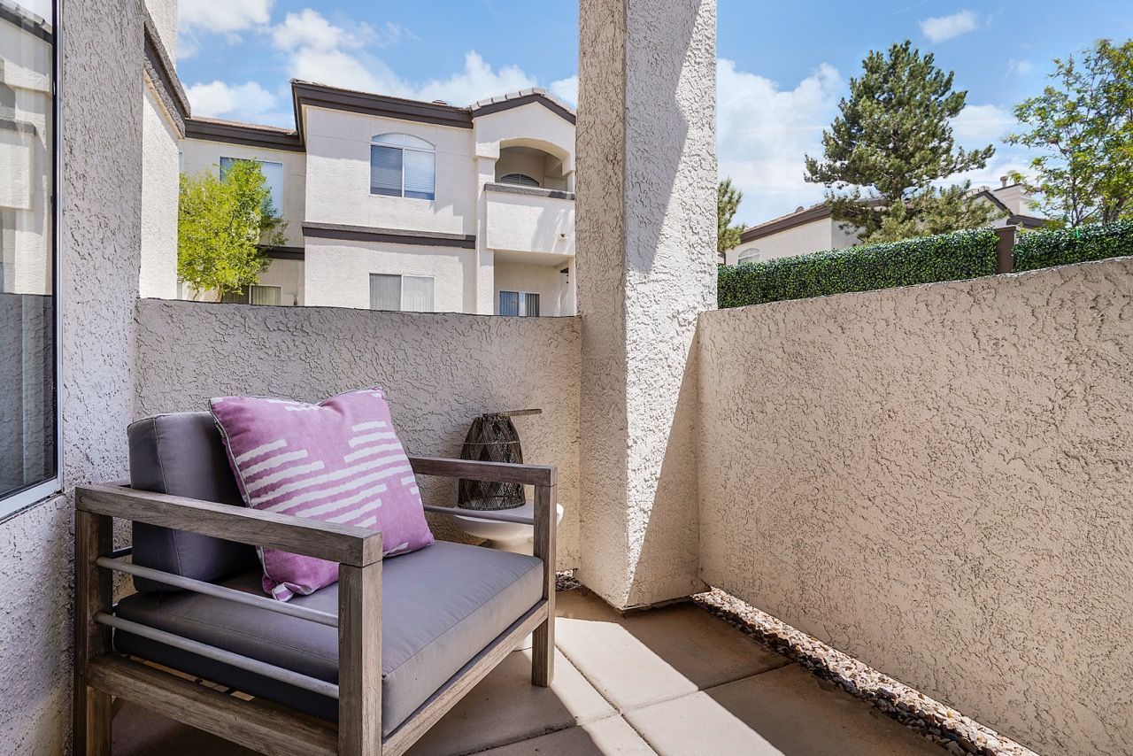 Small outdoor balcony with a wooden armchair and purple cushion against beige stucco walls at Broadstone Heights in Albuquerque, NM.