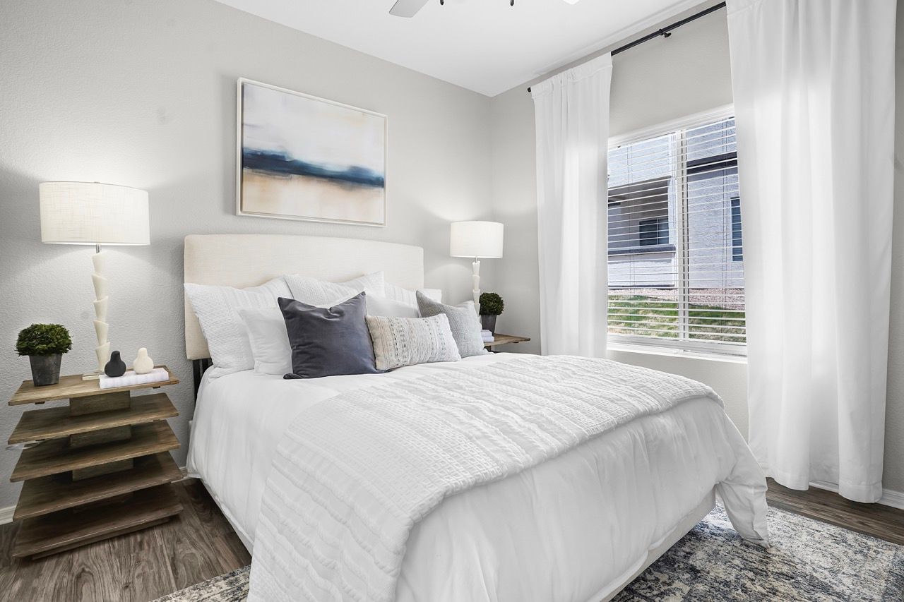 Bedroom with white bedding, two nightstands, lamps, and a large window with white curtains at Broadstone Heights in Albuquerque, NM.