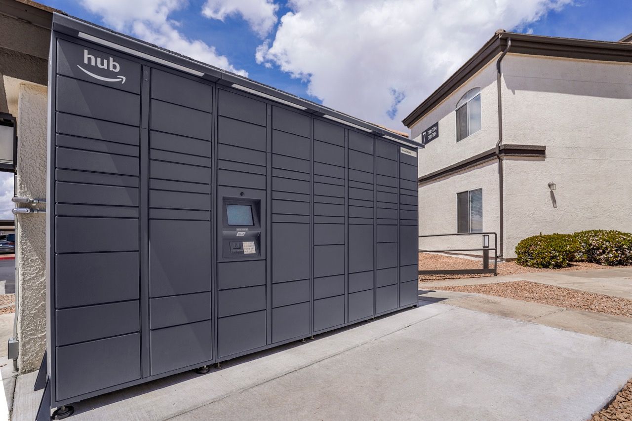 Exterior view of a long row of dark gray package lockers labeled 'hub' beside a building at Broadstone Heights in Albuquerque, NM.