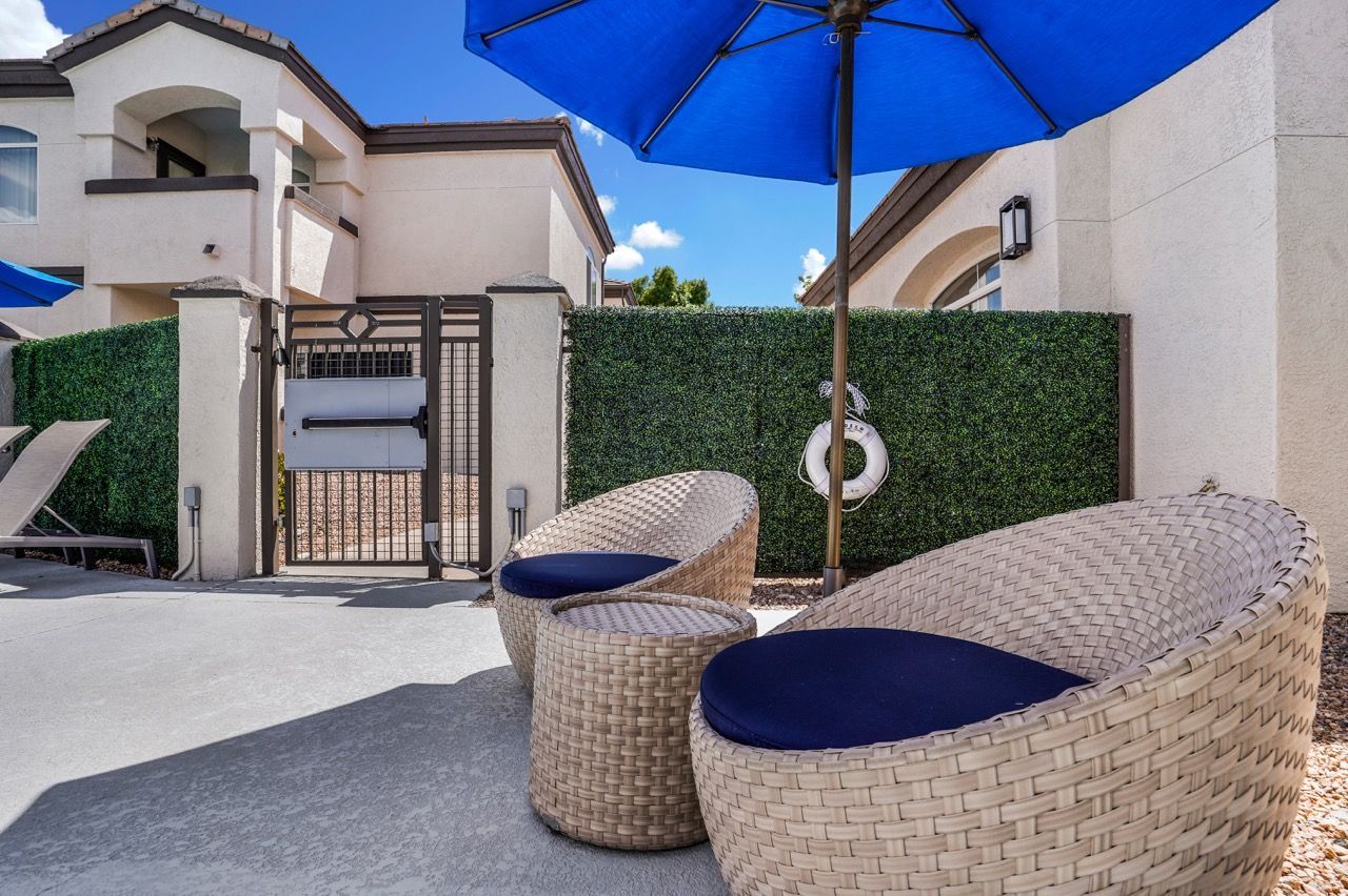 Outdoor communal patio with wicker lounge chairs, a blue umbrella, and a gated entry at Broadstone Heights in Albuquerque, NM.