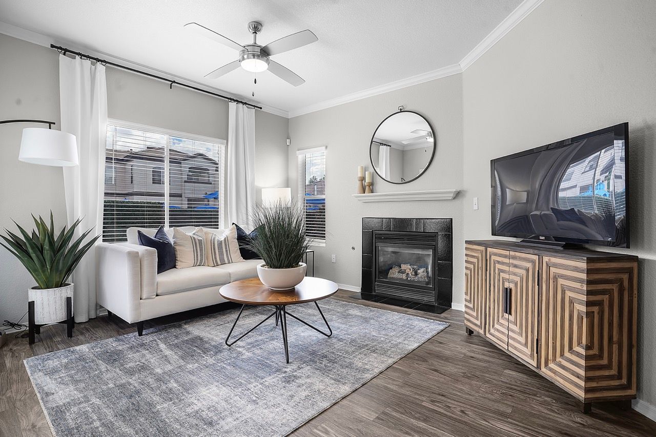 Living room with white sofa, fireplace, round mirror, ceiling fan, and TV on a wooden cabinet.