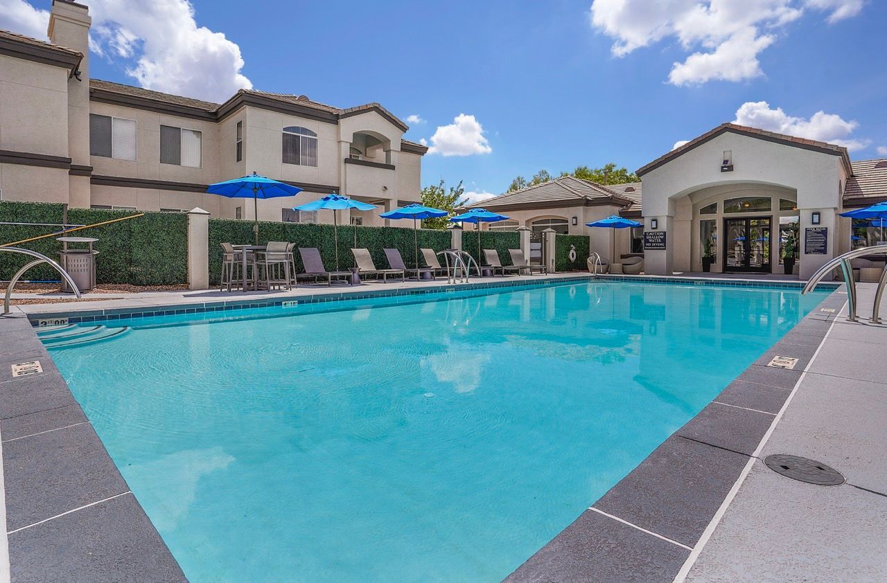 Outdoor apartment community pool with lounge chairs and blue umbrellas at Broadstone Heights in Albuquerque, NM.