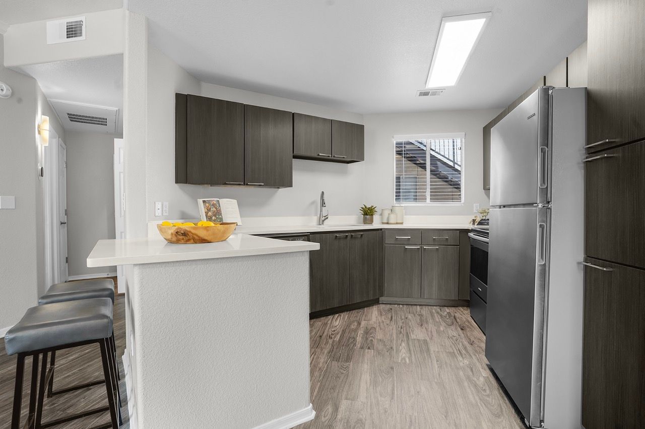 Modern apartment kitchen with dark wood cabinets, stainless steel fridge, and breakfast counter at Broadstone Heights in Albuquerque, NM.