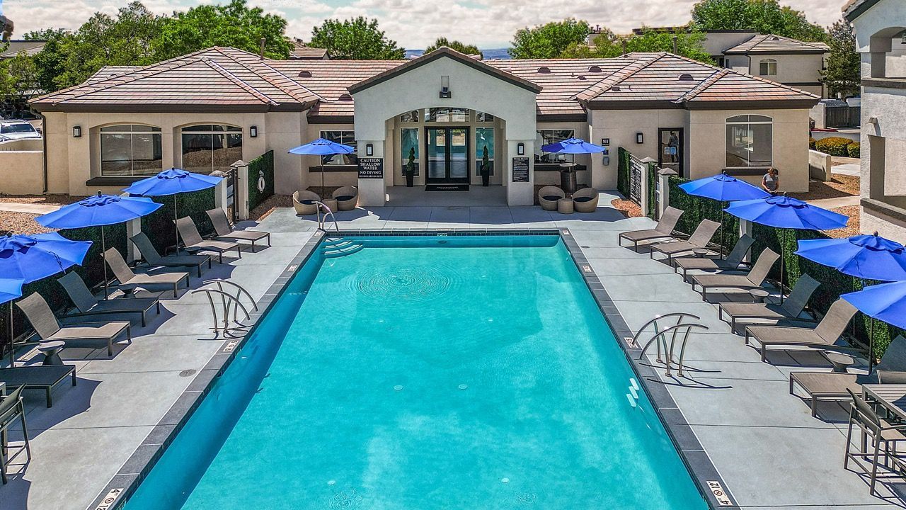 Rectangular pool area with lounge chairs and blue umbrellas at an apartment community at Broadstone Heights in Albuquerque, NM.
