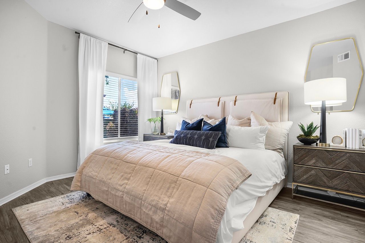 Bedroom in a contemporary apartment with a plush bed, nightstands, and a large window with white curtains at Broadstone Heights in Albuquerque, NM.