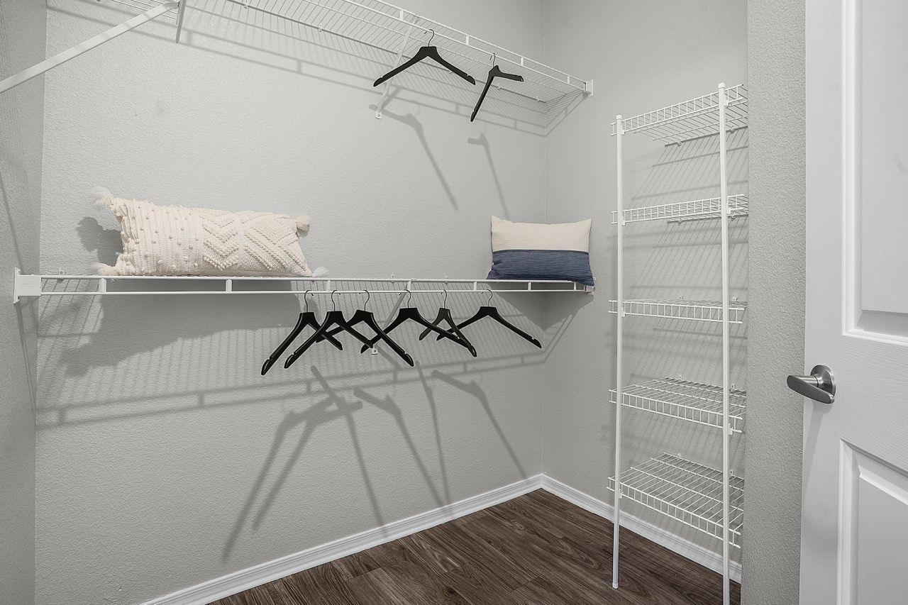Walk-in closet with white wire shelving, hanging rods, and a couple of decorative pillows at Broadstone Heights in Albuquerque, NM.