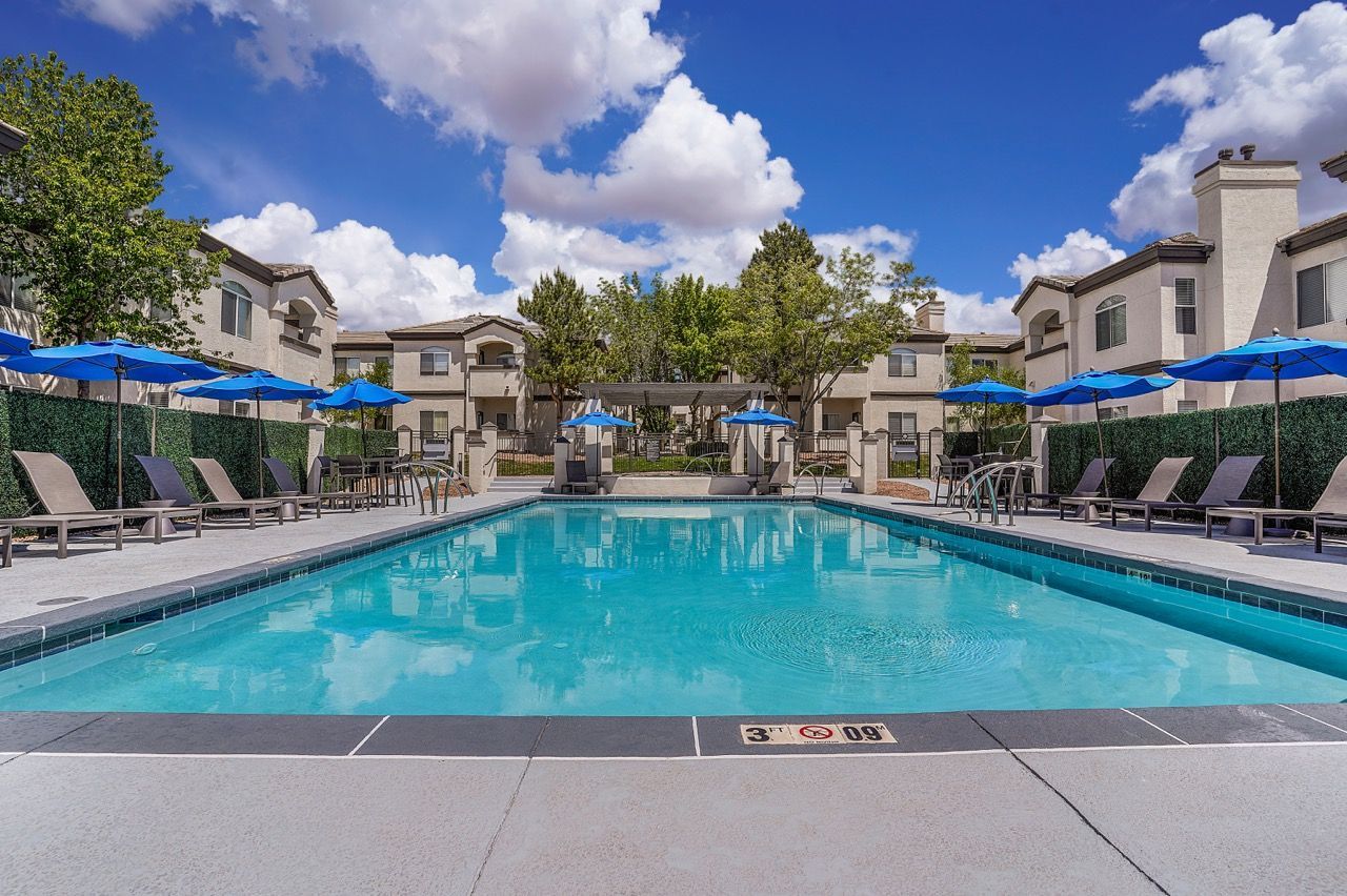 Outdoor apartment community pool with blue umbrellas and lounge chairs at Broadstone Heights in Albuquerque, NM.