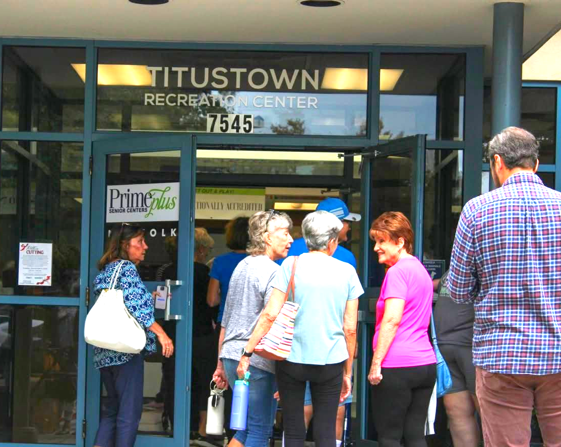 People entering Titustown Recreation Center. Building has glass doors, signage, and a blue awning.