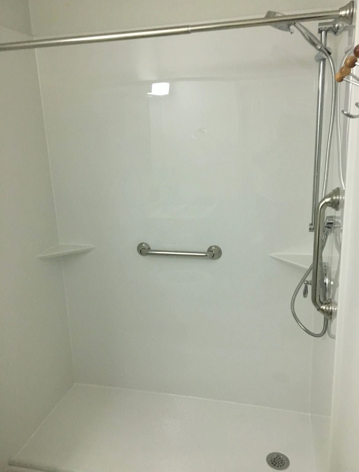 A white shower with a hand rail and a shower head.