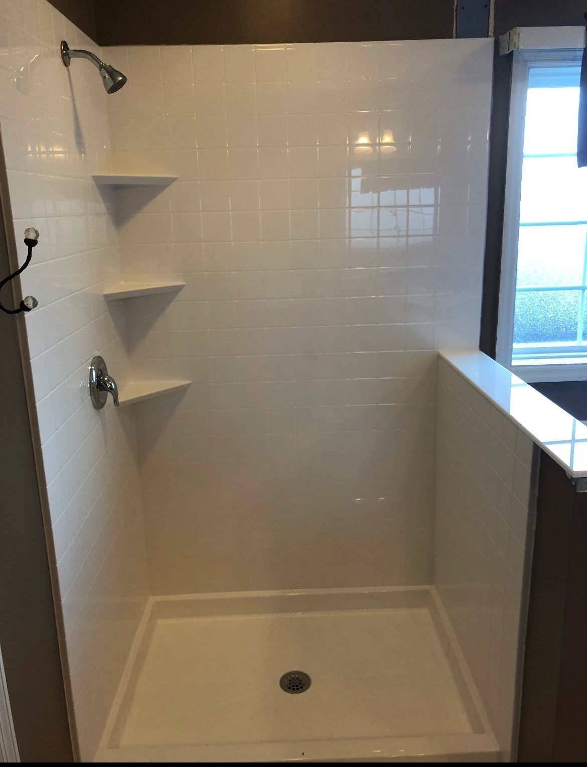 A white shower stall with a window in the background