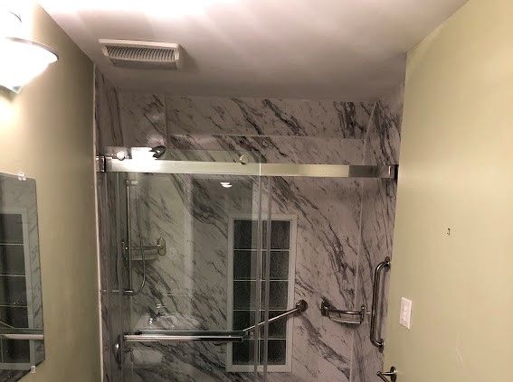 A bathroom with marble walls and a sliding glass shower door.