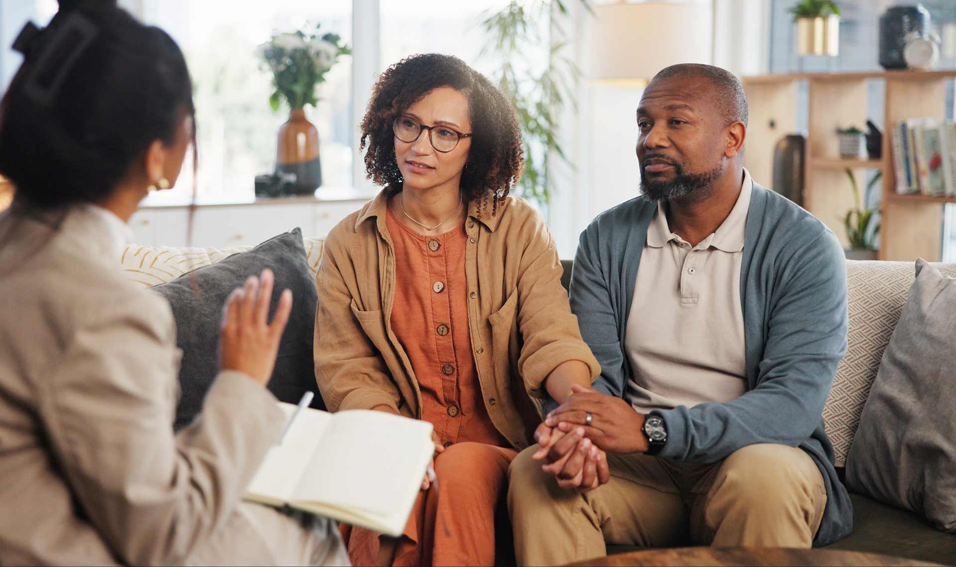 Couple holding hands, consulting with a person holding a notebook in a living room setting.
