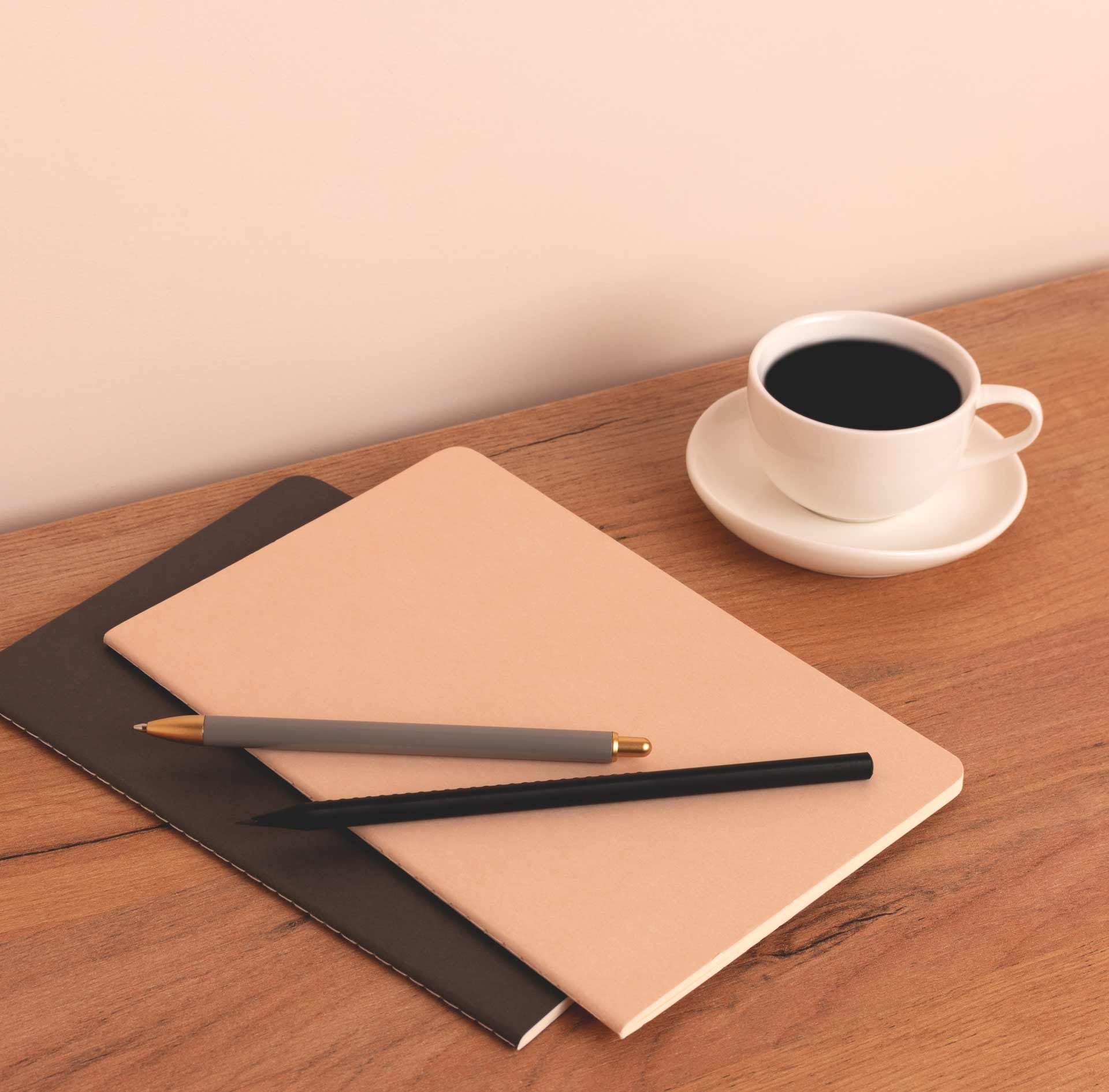Notebooks, pens, and coffee cup on a wooden table.