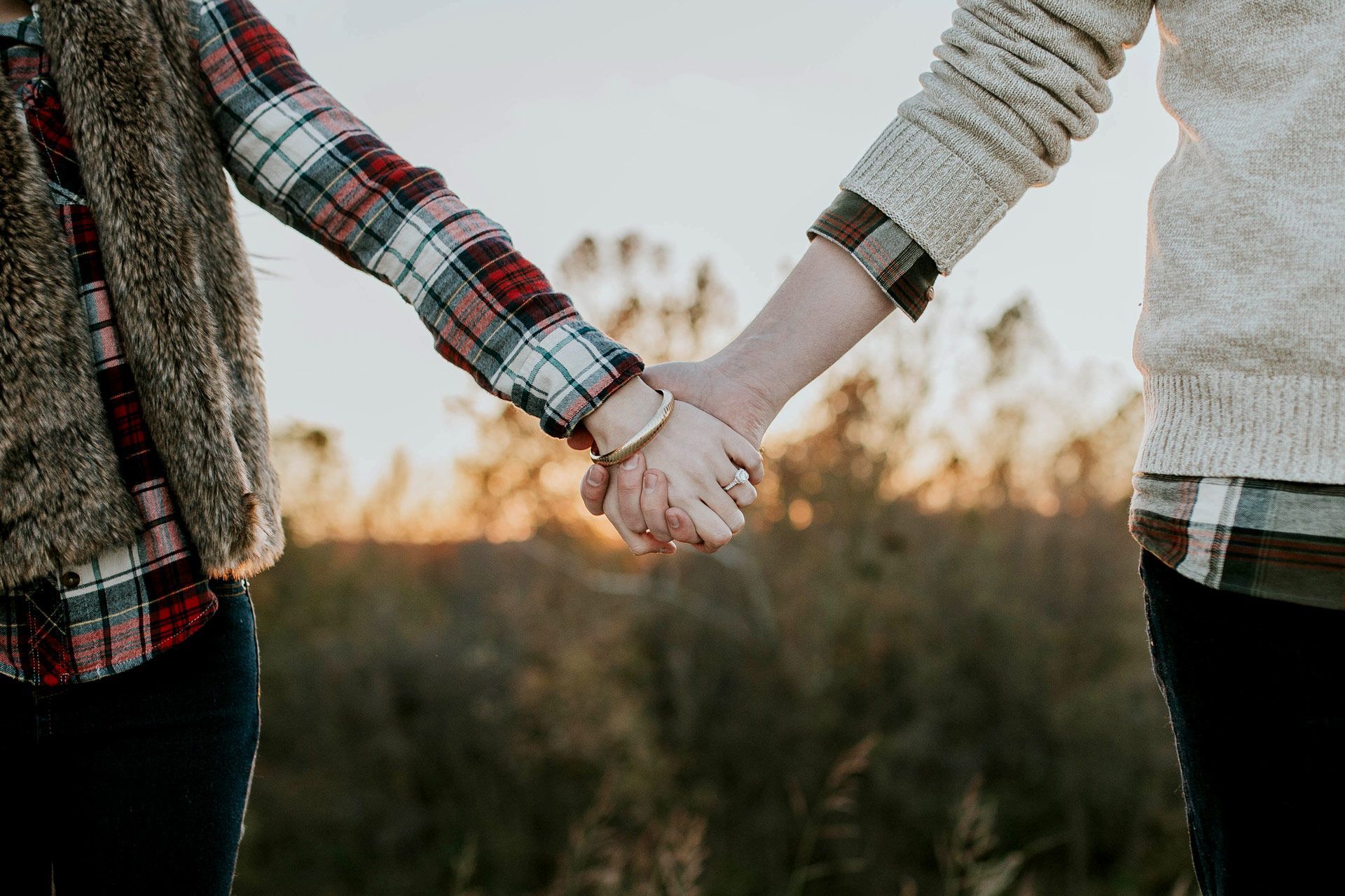 Two people holding hands outdoors at sunset.