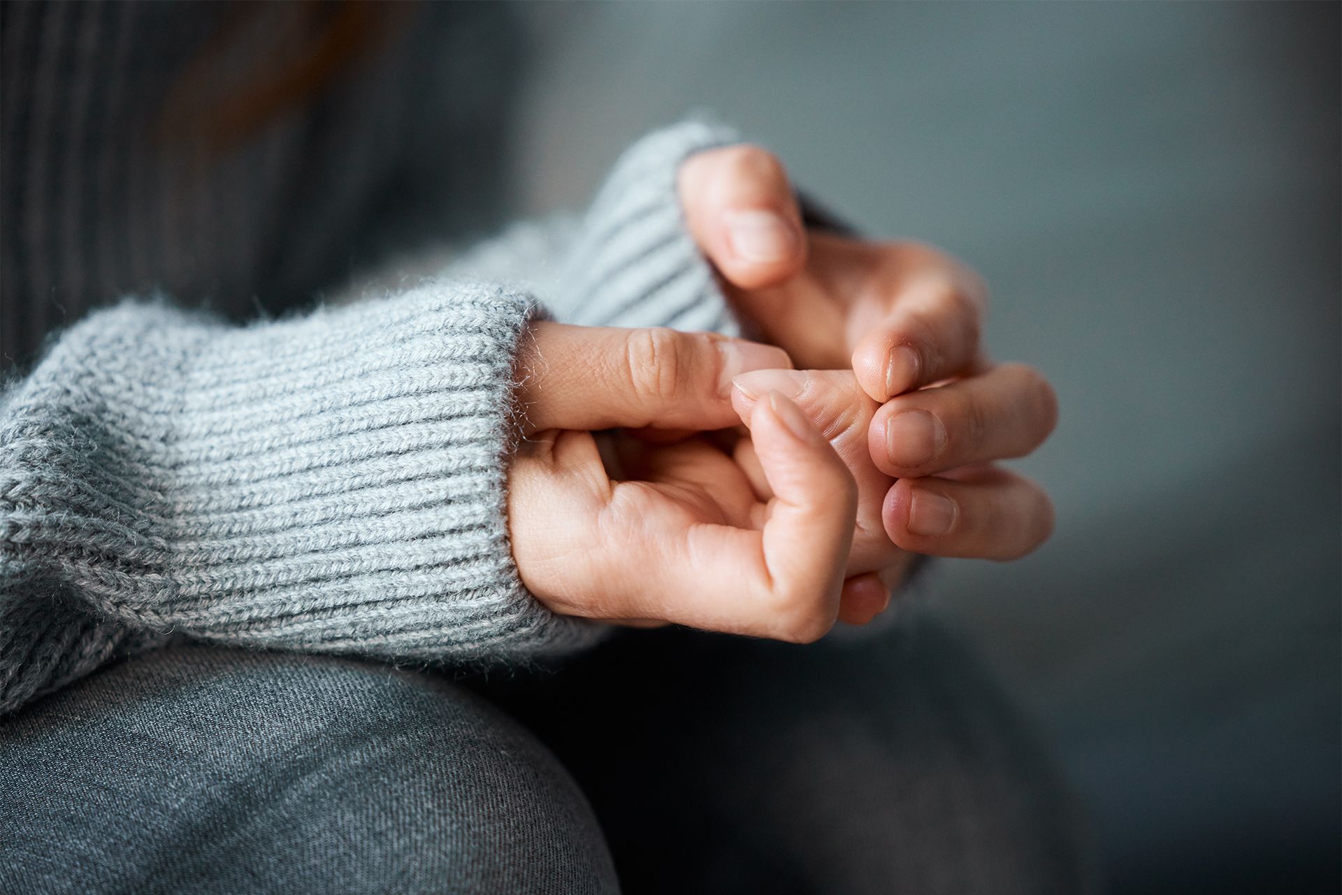 Person in gray sweater with hands clasped, knuckles visible.