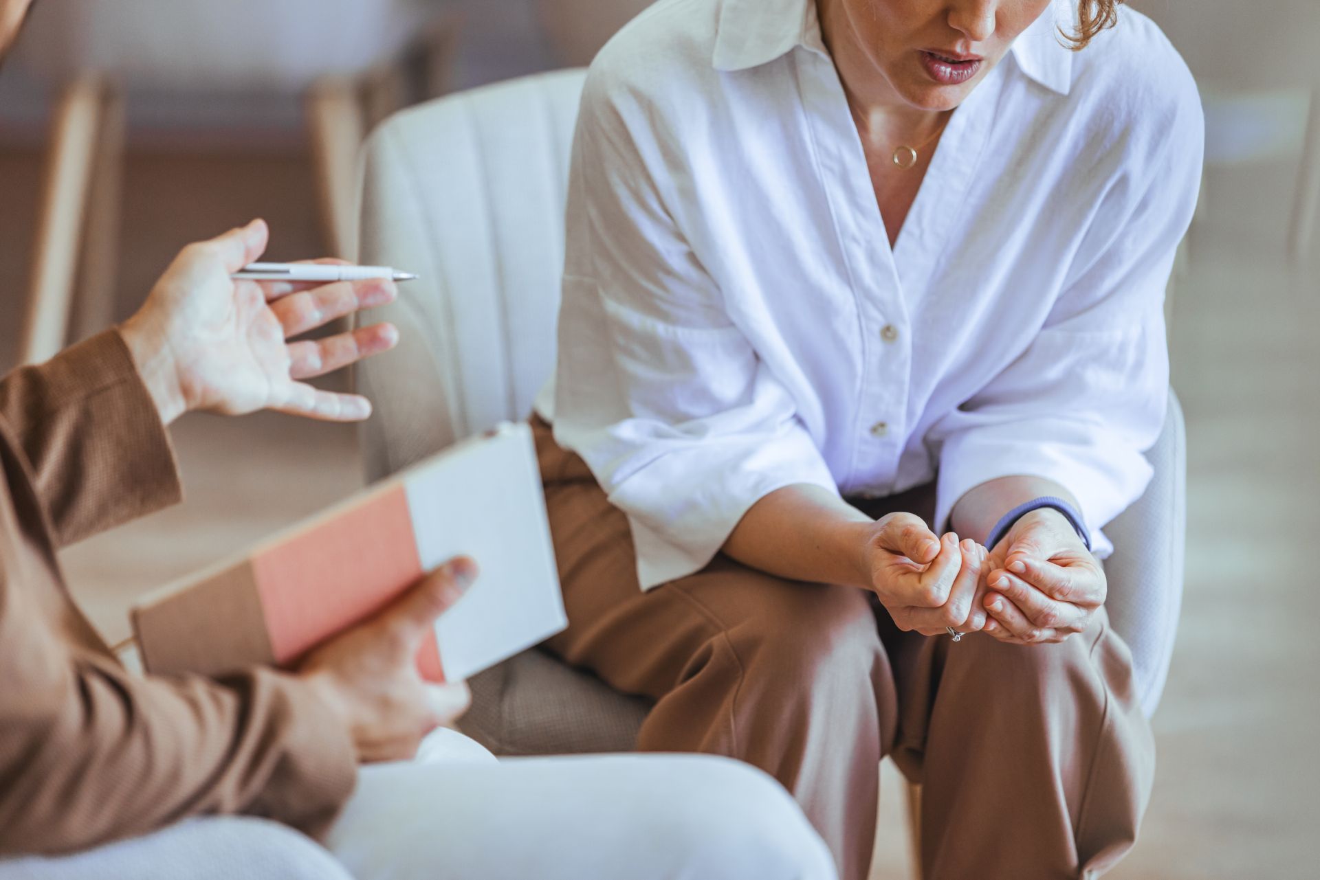 Therapist speaking with a seated client who looks down, holding hands in a calm 상담 setting