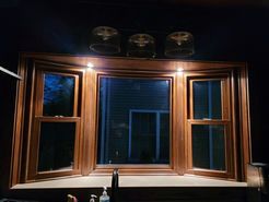 Wooden-framed bay window with three panes. Warm lighting illuminates the window from above.
