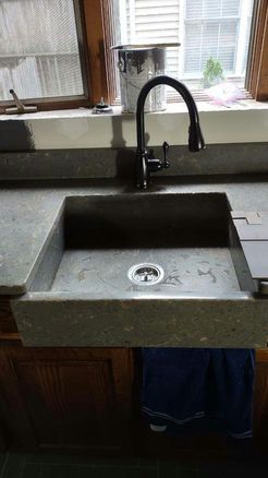 Dark sink basin with faucet on stone countertop, set in wood cabinetry, towel draped below.